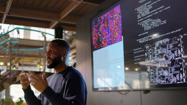 Человек проводит презентацию перед монитором, на котором отображаются сложные диаграммы и код.