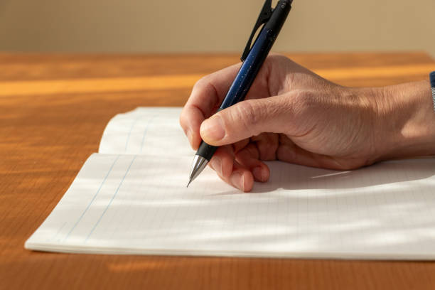 Рука держит ручку и пишет в блокноте на линованной бумаге.